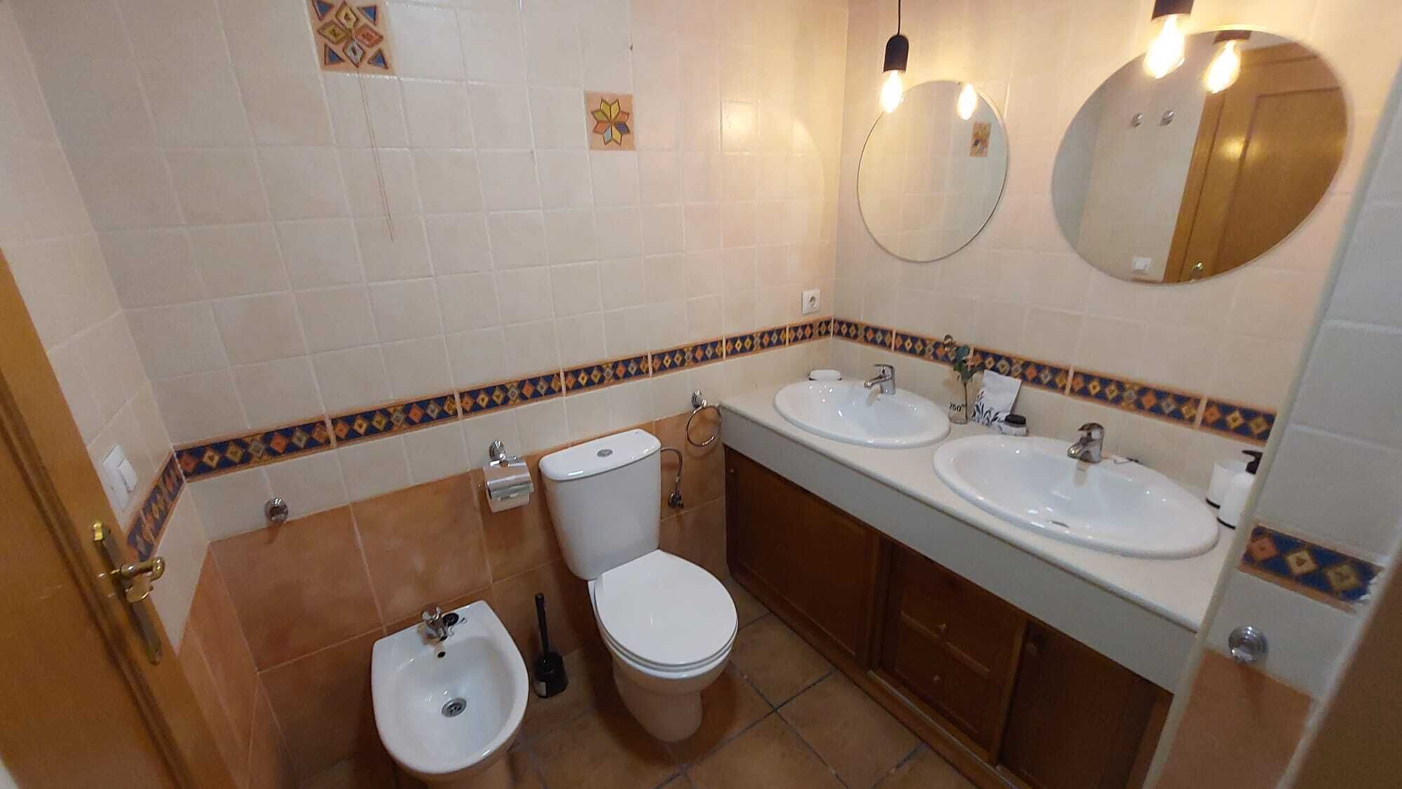 Un baño con dos lavamanos, un inodoro, un bidé y un espejo.