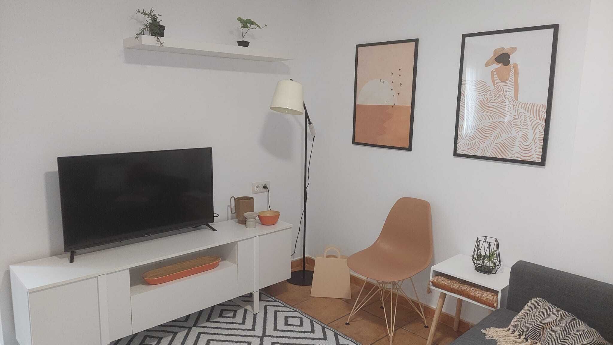Ein modernes Wohnzimmer mit einem Flachbildfernseher, einer Stehlampe, einem Sofa, einem Sessel und zwei gerahmten Kunstwerken an der Wand.
