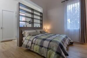 A bedroom with a bed, a bedside table with a lamp, a wardrobe, and a window with curtains.