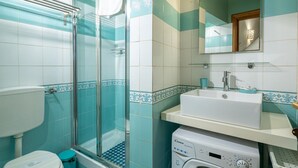 Ein Badezimmer mit Duschkabine aus Glas, Toilette, Waschmaschine und Waschbecken mit Spiegel darüber.