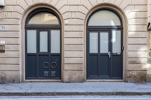 A building facade with two arched doors, numbered 79 and 81, with frosted glass panels and a metal door handle.