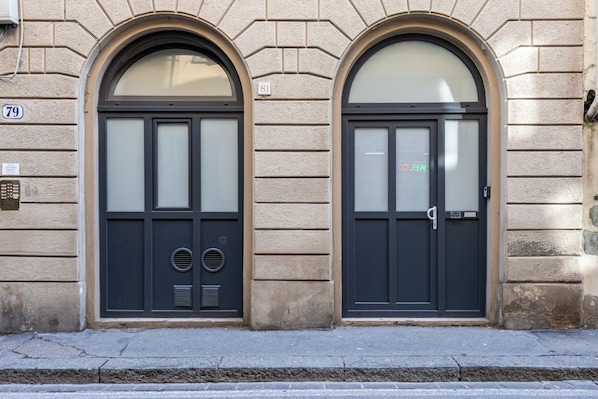 A building facade with two arched doors, numbered 79 and 81, with frosted glass panels and a metal door handle.