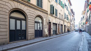 Eine schmale Straße gesäumt von historischen Gebäuden, mit Rundbogenfenstern und -türen, einem Gulideckel und einem Bürgersteig.