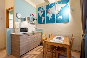 A compact kitchen with a microwave, sink, and wooden cabinets. There is a dining table with chairs and a world map on the wall.