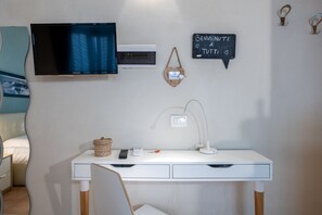 A white desk with a computer monitor, a desk lamp, a basket, and a remote control.