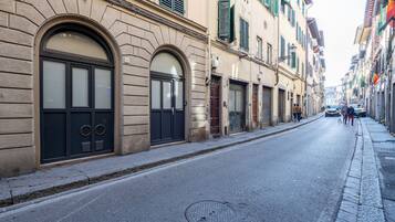 A narrow street lined with historic buildings, featuring arched windows and doors, a manhole cover, and a sidewalk.