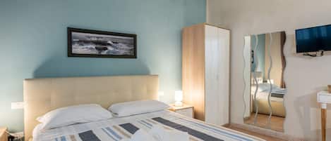 Una habitación de hotel con cama, mesita de noche, espejo y televisor.