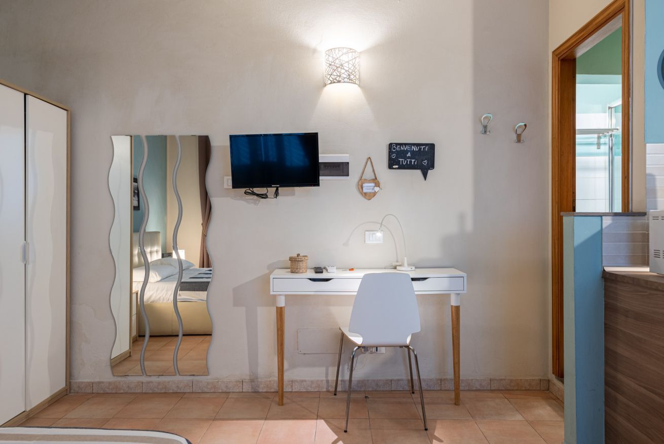 Ein modernes Zimmer mit Schreibtisch, Stuhl, Fernseher und Spiegel.