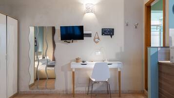 Ein modernes Zimmer mit Schreibtisch, Stuhl, Fernseher und Spiegel.