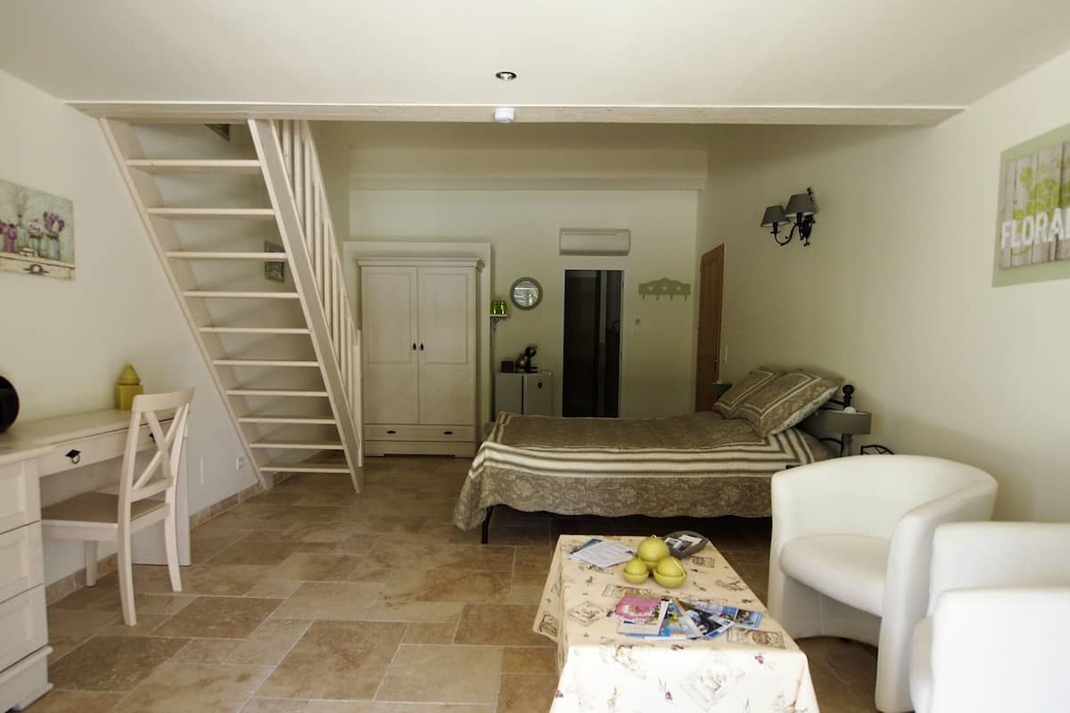 A bedroom with a bed, a desk, a chair, a staircase, and a door.