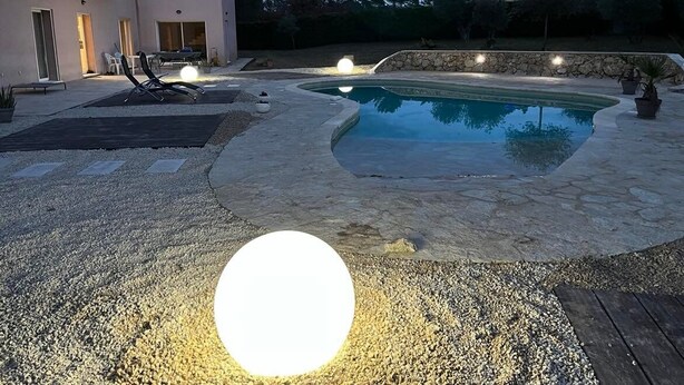 Una piscina con cubierta de piedra, una silla de descanso y un edificio pequeño al fondo.