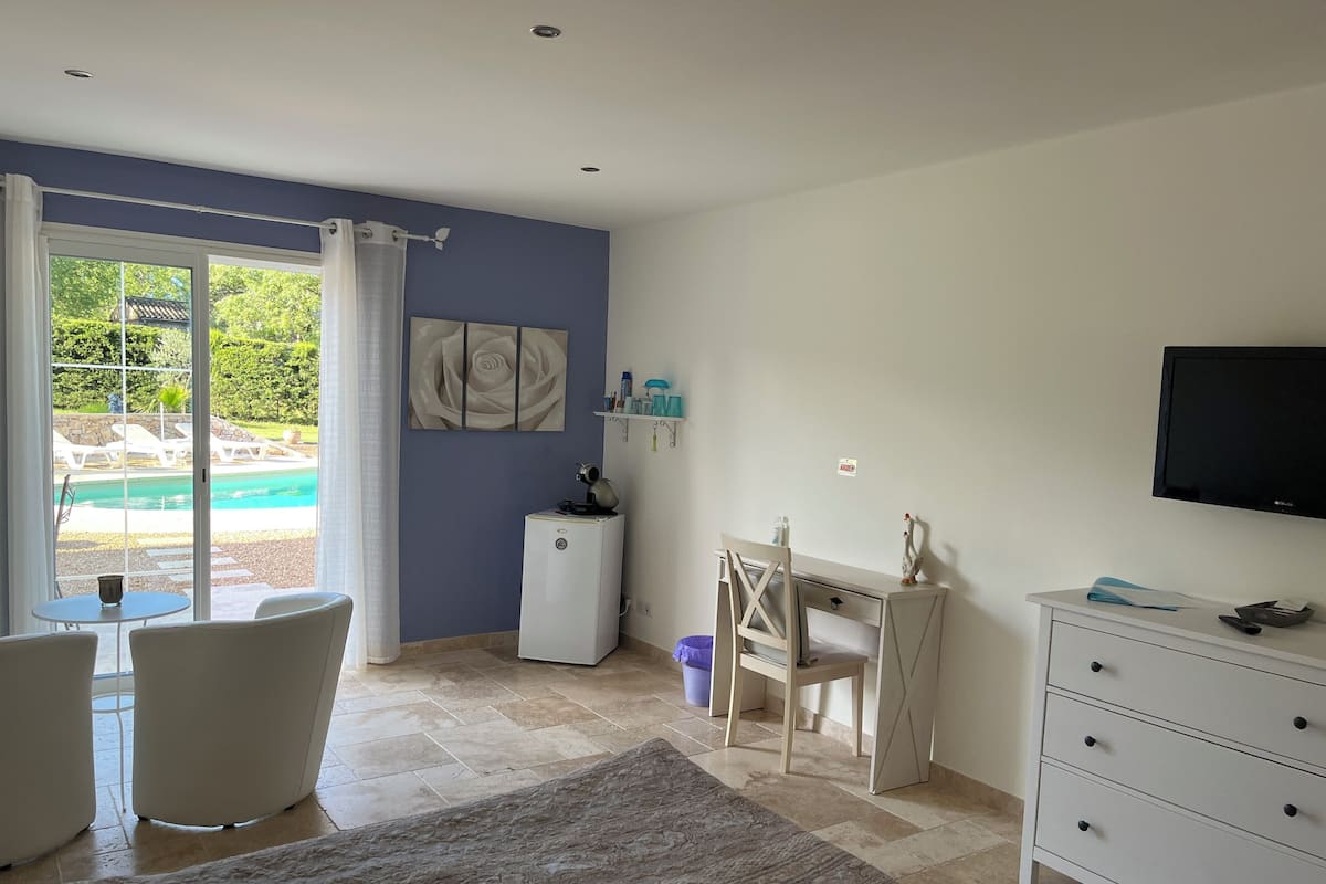 A room with a pool view, a desk, a chair, a TV, and a small cabinet.