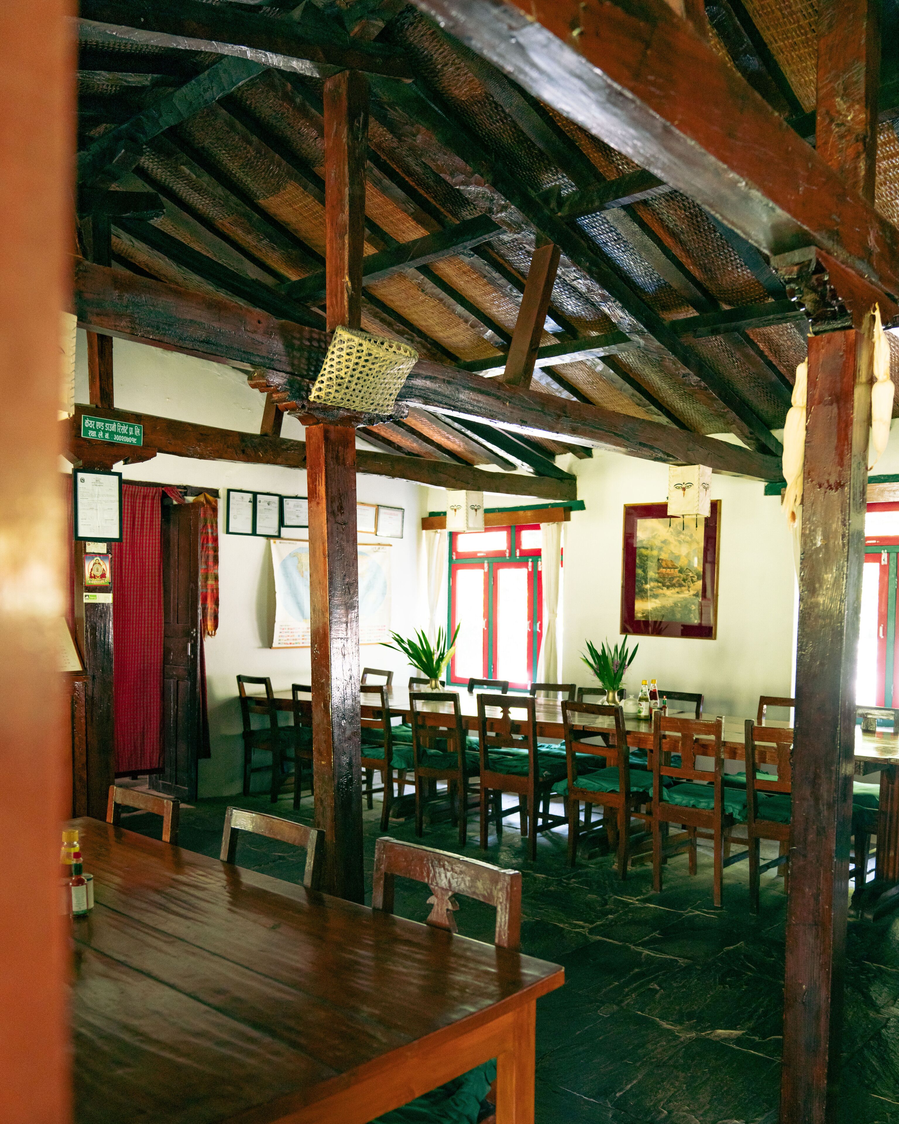 A rustic dining area with wooden tables and chairs, a thatched ceiling, and a sign in a foreign language.