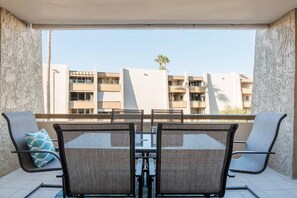 Un balcon avec une table et des chaises, une vue sur un ensemble d’immeubles et un ciel dégagé.