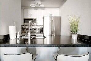 A modern kitchen with stainless steel appliances, a black countertop, and white cabinetry.