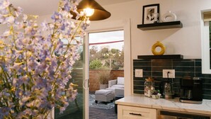 A modern kitchen with a coffee machine, a shelf with decorative items, and a view of the outdoor patio area.