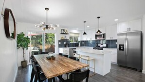 A modern kitchen with a central island, stainless steel appliances, and black pendant lighting.