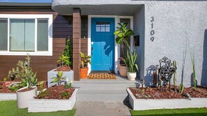 A modern house with a blue door, numbered 3109, and a well-maintained front yard with various plants.