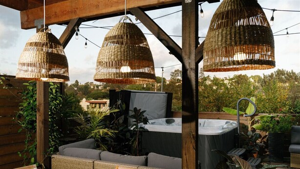 An outdoor patio with wicker furniture, a hot tub, and hanging wicker lamps.