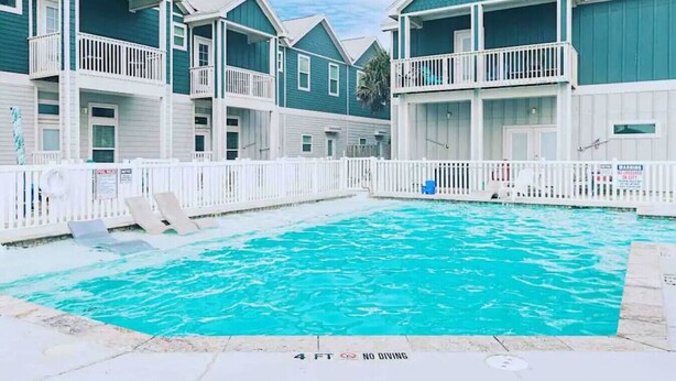 Una piscina rodeada de edificios de dos pisos con balcones, barandillas blancas y un letrero que indica que está prohibido bucear.
