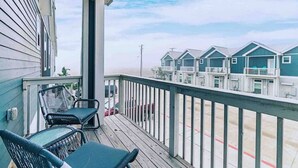 Una terraza de madera con dos sillas y una mesa, con vistas a una hilera de casas de playa con balcones.