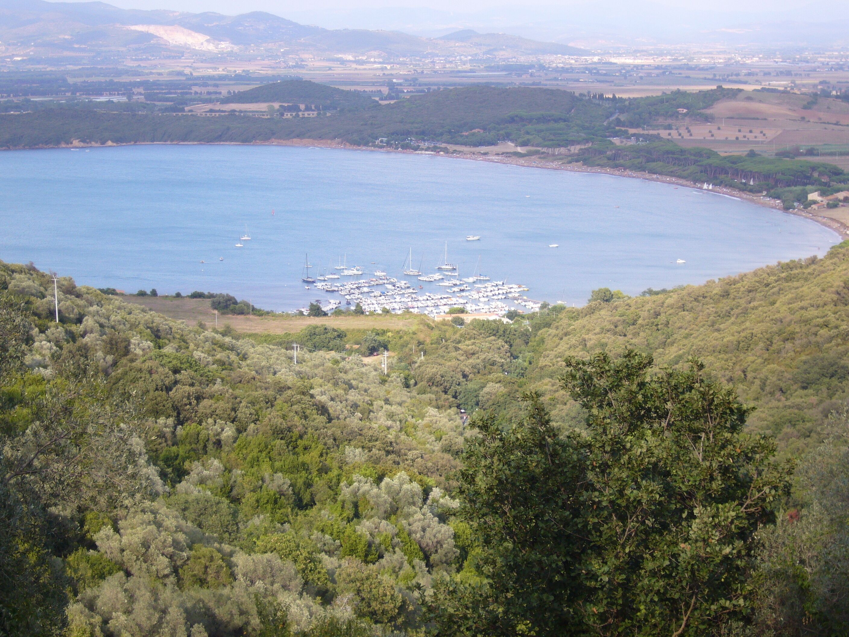 Un paysage côtier avec un port de plaisance, entouré d’une végétation luxuriante et de collines.