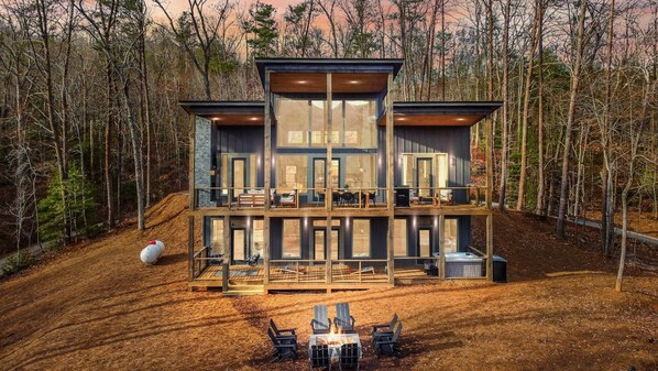 A modern multi-story cabin with large windows, a deck, and outdoor seating. - Weaver Creek Lodge ~ Near Downtown Blue Ridge ~ Hot Tub, Fire Pit, & Views! (Blue Ridge)