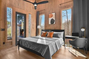 A modern bedroom with a large bed, a desk, and a chair. There are multiple windows and a fireplace. - Weaver Creek Lodge ~ Near Downtown Blue Ridge ~ Hot Tub, Fire Pit, & Views! (Blue Ridge)