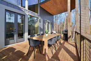An outdoor deck with a wooden table and chairs, large sliding glass doors, and a grill. - Weaver Creek Lodge ~ Near Downtown Blue Ridge ~ Hot Tub, Fire Pit, & Views! (Blue Ridge)