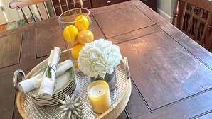 A dining table set with a fruit bowl, napkins, a candle, and a decorative tray.
