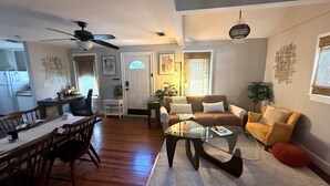 Un salon avec un coin repas, un ventilateur de plafond et une cuisine en arrière-plan.