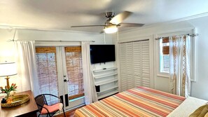 A hotel room with a bed, a desk with a lamp, a television mounted on the wall, and a ceiling fan. - Downtown Cottage | Walk Everywhere, Park once (St Petersburg)
