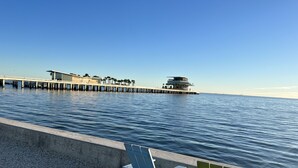 Une vue sur le front de mer, avec une jetée qui s’avance dans l’eau, des bâtiments modernes et un ciel dégagé.