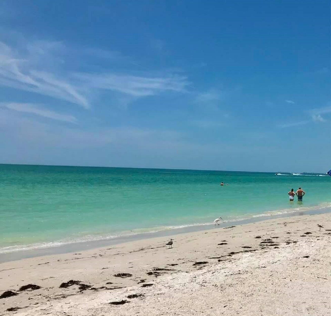 Una playa con agua turquesa cristalina, una orilla arenosa y algunas personas caminando por la orilla.