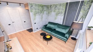 Una sala de estar moderna con un sofá verde, una mesita redonda con fruta y una lámpara de pie.