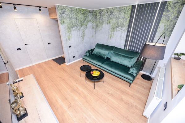 A modern living room with a green sofa, a small round table with fruit, and a floor lamp.
