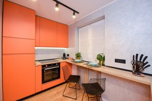 A modern kitchen with orange cabinets, a wooden countertop, and two black wire chairs.