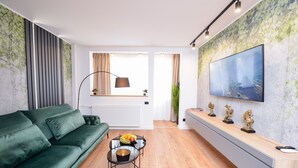 Una sala de estar moderna con un sofá verde, una mesa de centro de vidrio con fruta, un televisor en la pared y un mueble de madera.
