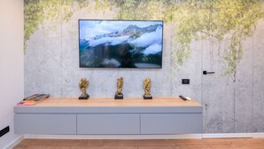Habitación moderna con un televisor de pantalla plana grande montado en una pared texturizada, una mesa consola de madera con objetos decorativos y una puerta con pomo.