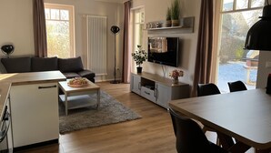 Ein modernes Wohnzimmer mit Sofa, Fernseher, Esstisch und einer kleinen Küchenzeile.