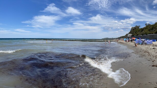 Ein Strand mit blauem Himmel, Wellen und einem hölzernen Steg, der sich ins Wasser erstreckt.