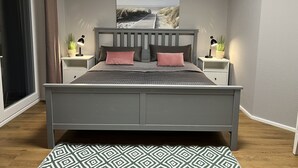 Ein Schlafzimmer mit einem grauen Bett, zwei Nachttischen mit Lampen, einem großen Bild an der Wand und einem gemusterten Teppich.