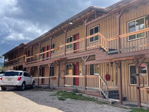 A two-story wooden building with balconies, a red door, and a car parked in front.