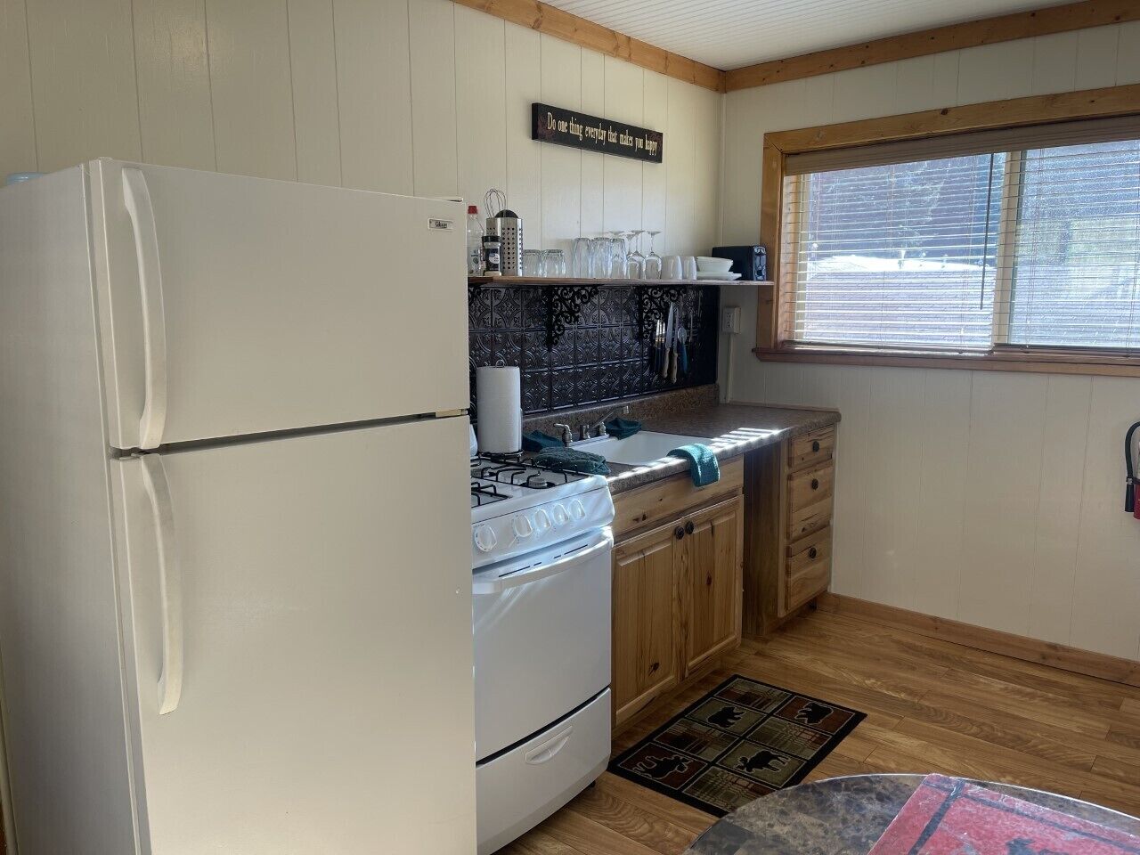 A kitchen with a refrigerator, stove, sink, wooden cabinets, and a window.