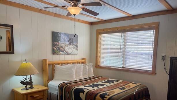 A bedroom with a bed, a nightstand with a lamp, a ceiling fan, a window with blinds, and a painting on the wall. - Red River Condo #4 near Main Street (Red River)