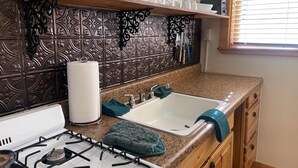 A kitchen with a gas stove, two sinks, a paper towel dispenser, and a window with blinds. - Red River Condo #4 near Main Street (Red River)