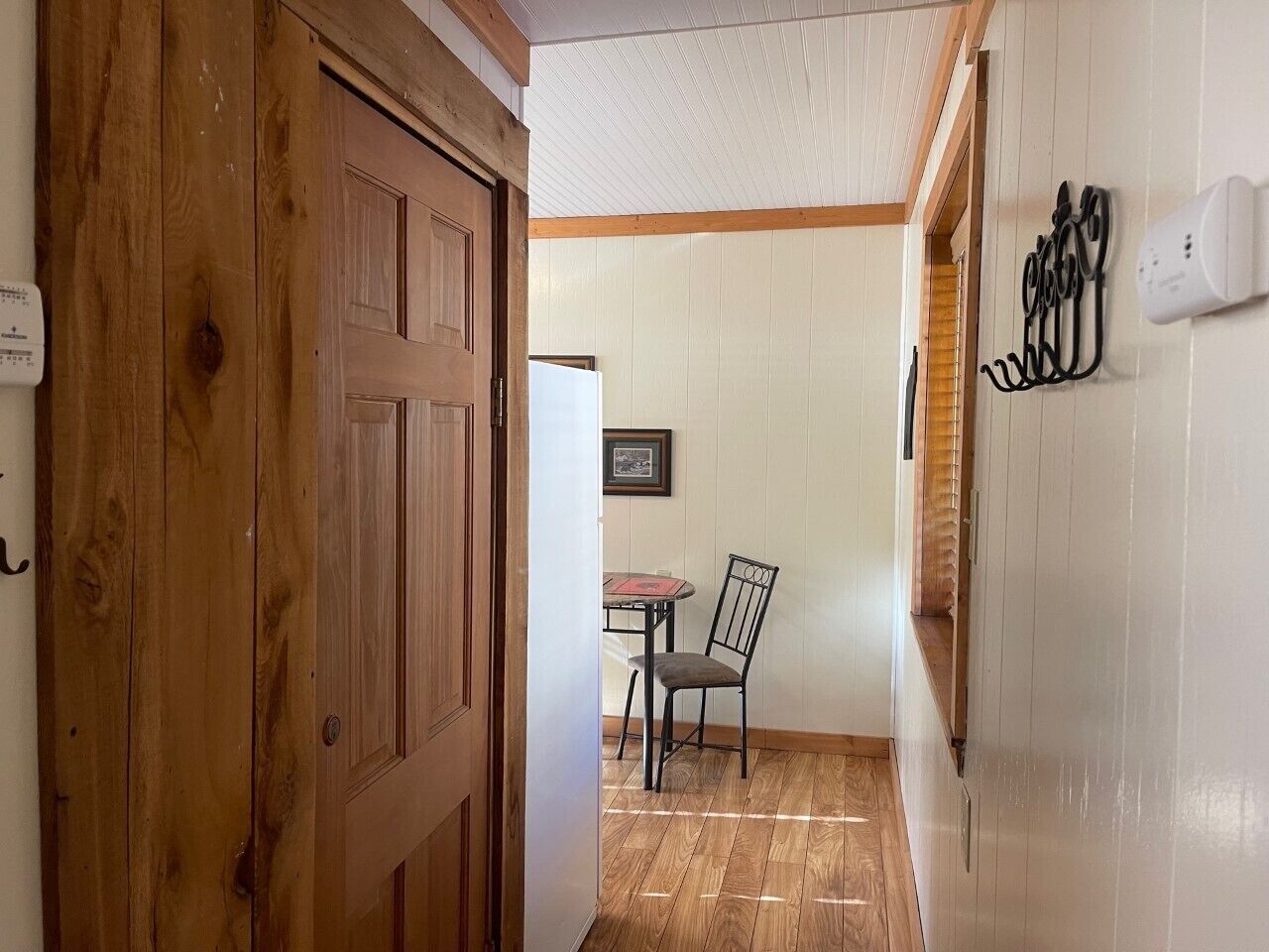 A hallway with a wooden door, a table with a chair, and a white wall with a picture frame.