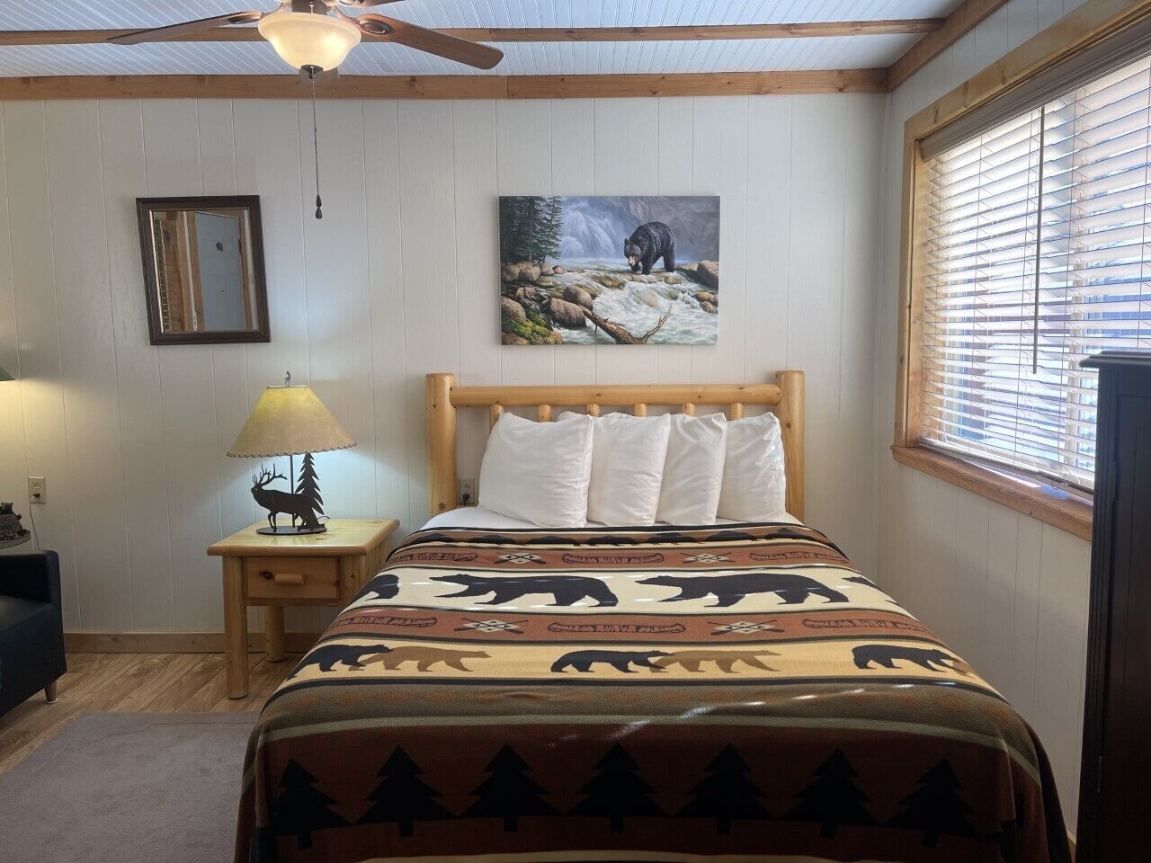 A bedroom with a bed, a nightstand, a lamp, a painting, and a window with blinds.