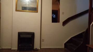A room with hardwood flooring, a fireplace, a staircase, and a wall-mounted mirror.