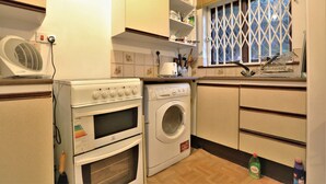 A compact kitchen with a washing machine, oven, and a fan.